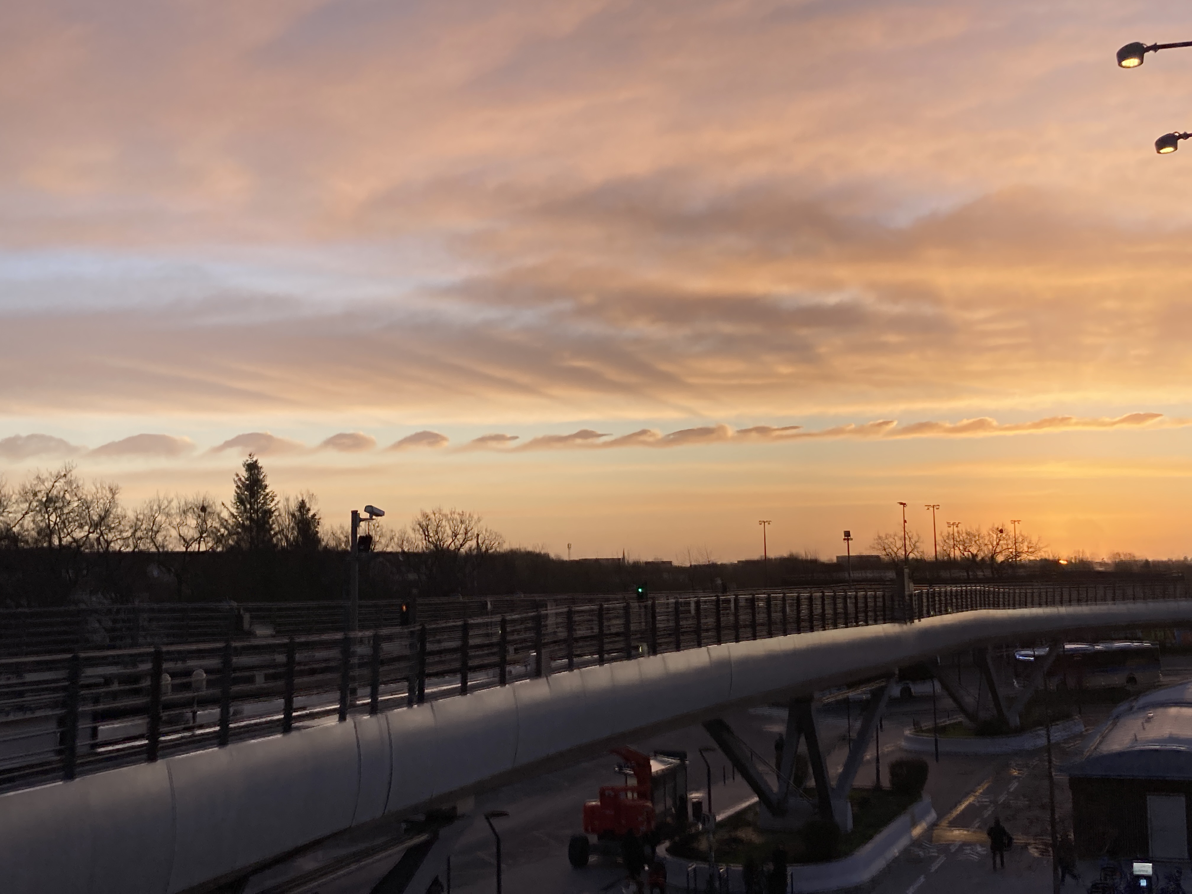 Photo de l'aurore au-dessus des rails du métro aérien de la Poterie. Une ligne parfaitement droite de tout petits nuages en forme de vagues surplombe l'horizon.