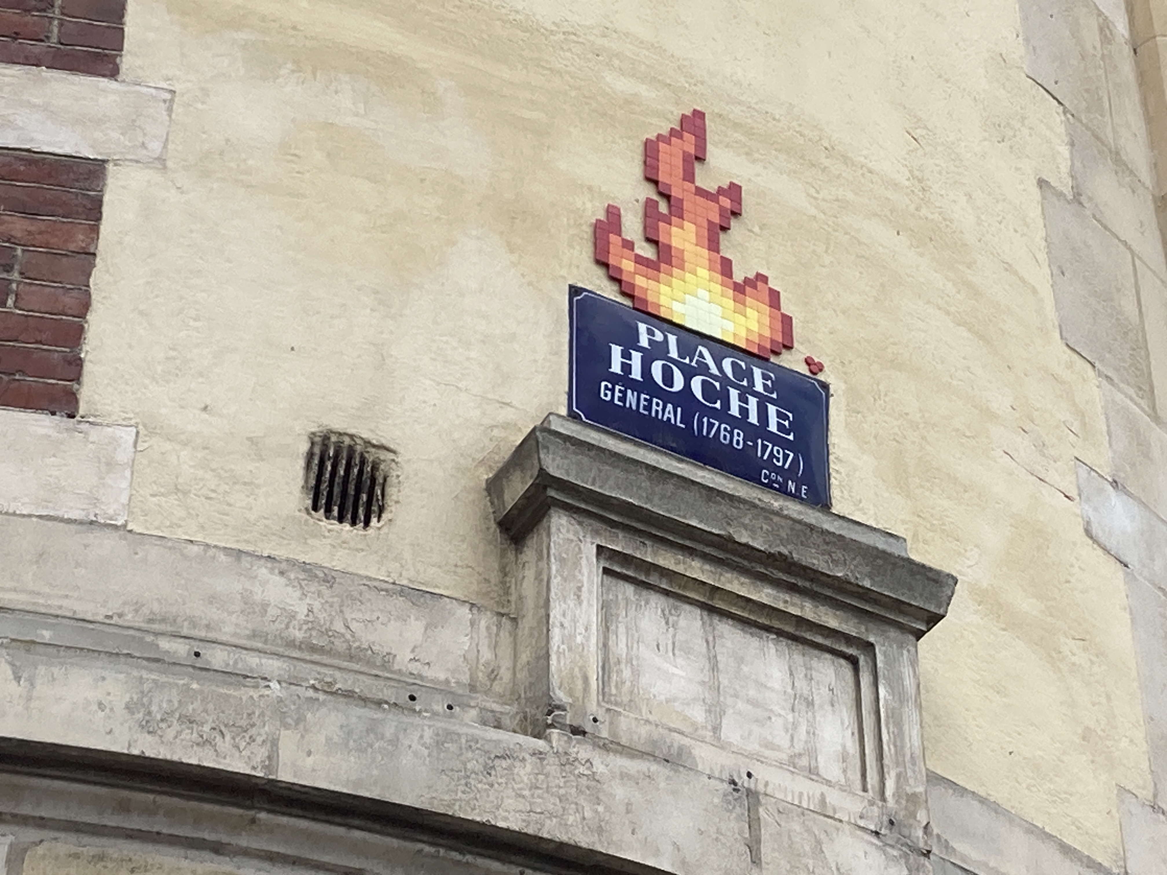 Plaque de rue indiquant la Place Hoche. Une mosaïque a été collée au-dessus pour dessiner une grossse flamme en pixel-art.